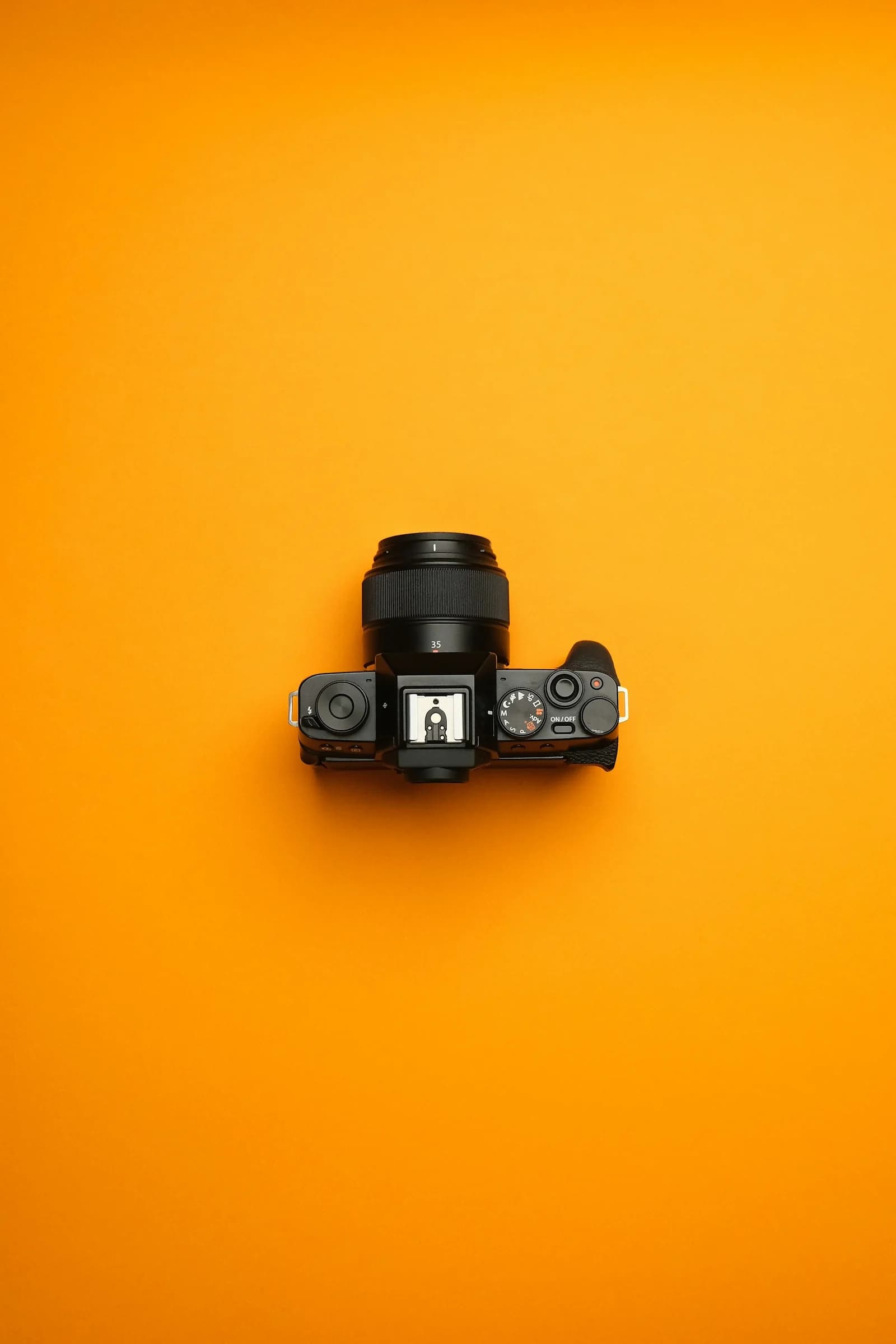 Canlı turuncu fonda yukarıdan çekilmiş siyah fotoğraf makinesi
